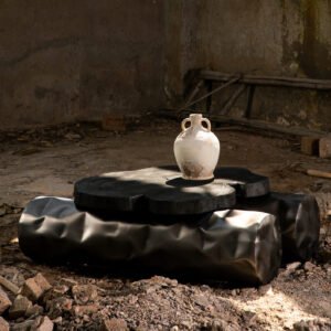 Sculptural centre table with stainless steel base in matt gunmetal finish resembling two wooden logs and a burnt wood top in a rustic setting.