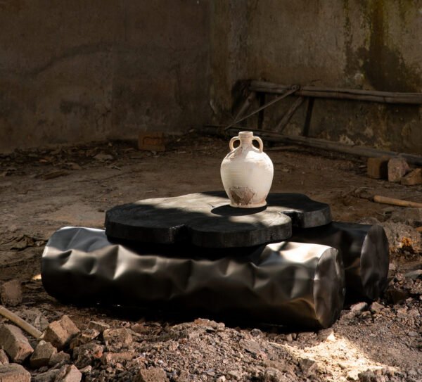 Sculptural centre table with stainless steel base in matt gunmetal finish resembling two wooden logs and a burnt wood top in a rustic setting.