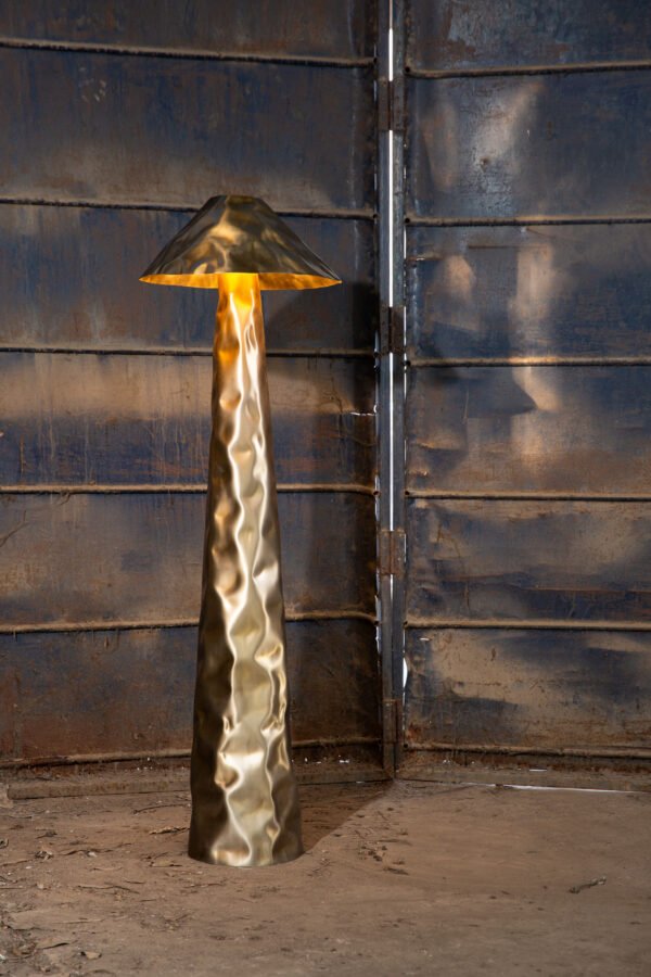 Stainless steel floor lamp in matt gold finish against a metallic door.