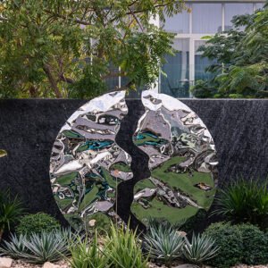 Stainless steel floor sculpture in a garden surrounded by plants