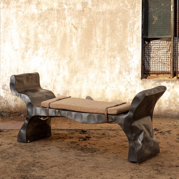 Organic form stainless steel sculptural bench with raffia seating adorned with belts to hold the seating to the bench.