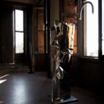 Modern stainless steel floor sculpture in an old room with windows.