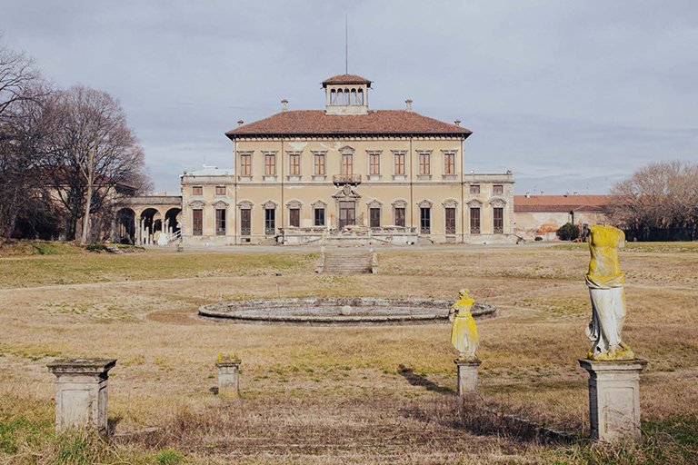 Villa surrounded by gardens with a fountain and stone sculptures.