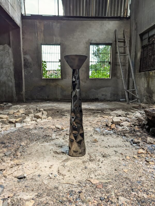 Pedestal in stainless steel with a sculptural texture in a factory setting.