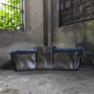 Frontal view of the Triolith Bench, highlighting its shiny stainless steel body and plush faux fur seat, set against an outdoor backdrop to showcase its design.