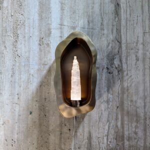 Front view of the Sigil Crest Wall Sconce showing the sleek stainless steel design and translucent selenite, mounted on a concrete wall.