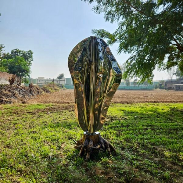 Stainless steel floor sculpture in an outdoor setting next to a tree.