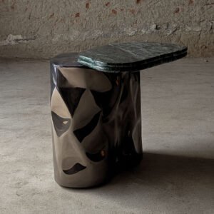 Profile view of the Colgada Side Table showing sculptural stainless-steel volume and cantilevered marble top