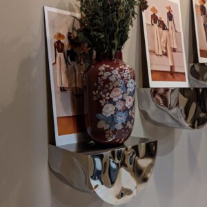 Close-up of the polished stainless-steel Tronco Shelf displaying a floral ceramic vase and framed artwork.